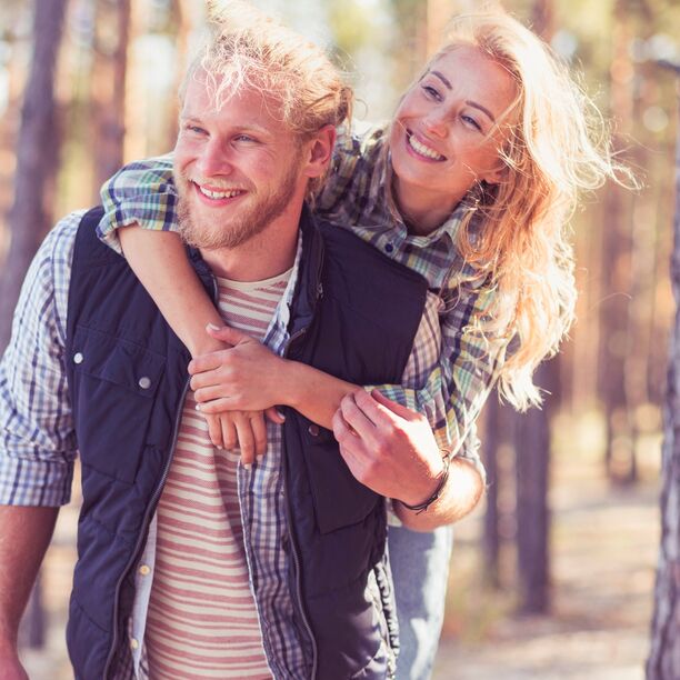 Ein Paar läuft durch den Wald, er trägt sie huckepack
