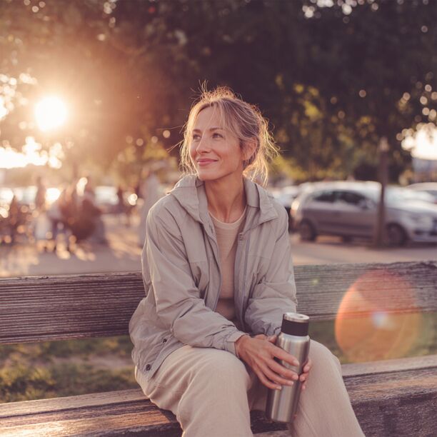 Eine Frau sitzt mit einem Kaffee auf der Bank