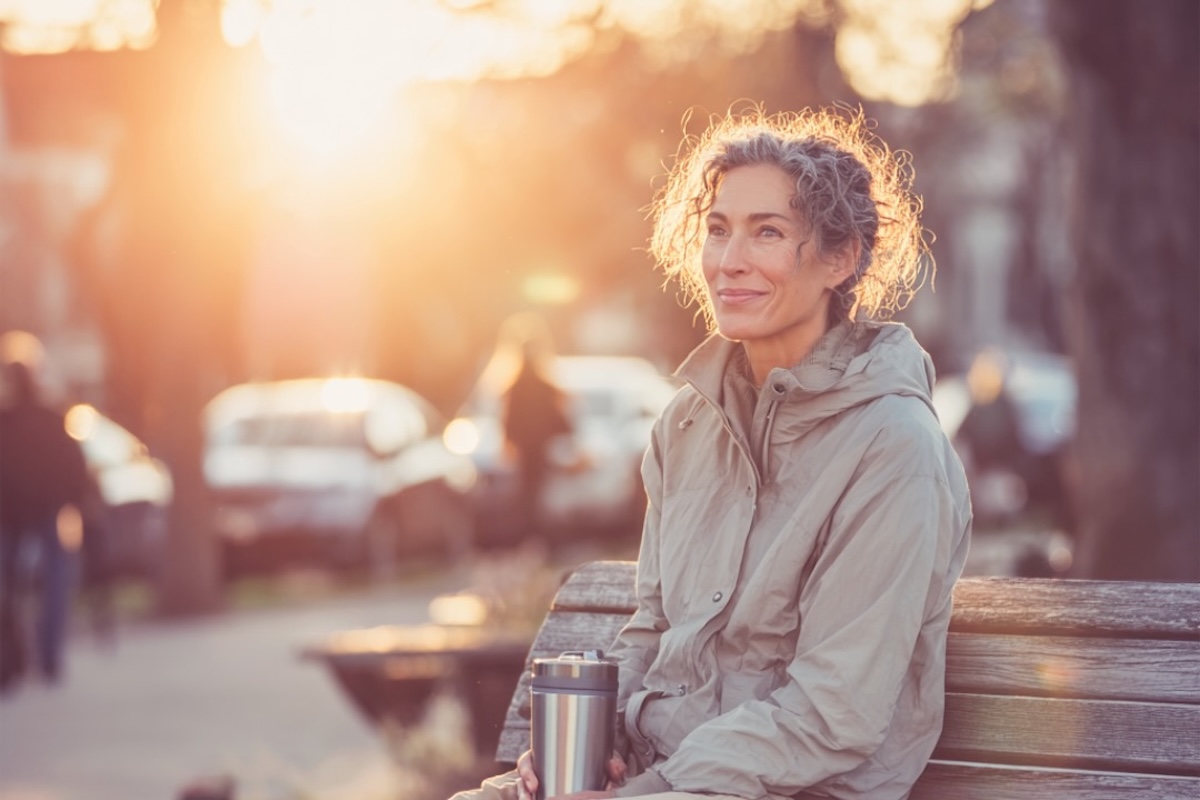 Eine Frau sitzt mit einem Kaffee auf der Bank