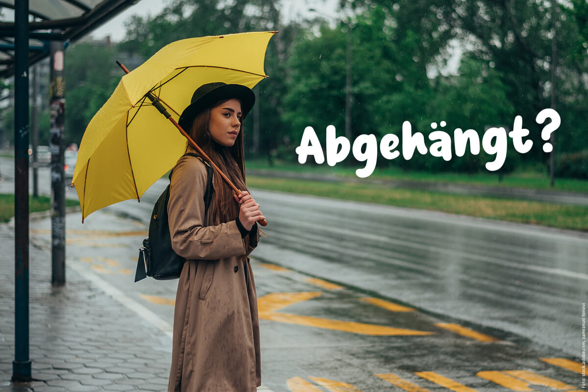 Frau steht mit gelbem Regenschirm an der Haltestelle während es regnet.